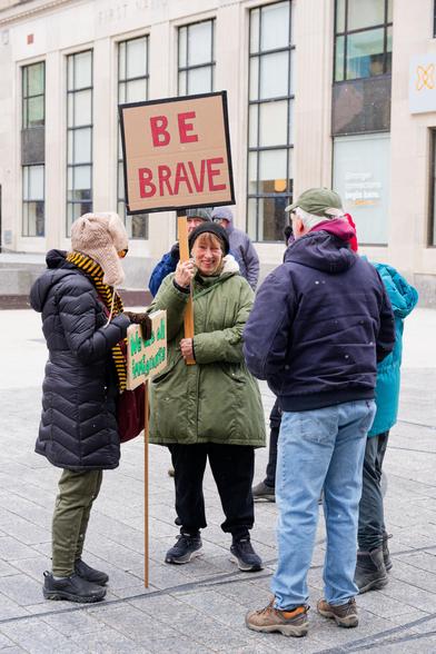 Woman stands with "Be Brave" sign surrounded by friends before No Kings protest last weekend in Ithaca