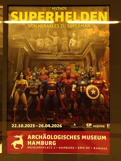 A poster advertising the exhibition. A crowd of US American superheroes is shown in front of a temple-like building, with the Graeco-Roman gods watching from above. The gods are depicted as white statues. A yellow headline reads: "Mythos Superhelden, von Herakles zu Superman", in English "Mythos Superheroes, from Heracles to Superman".