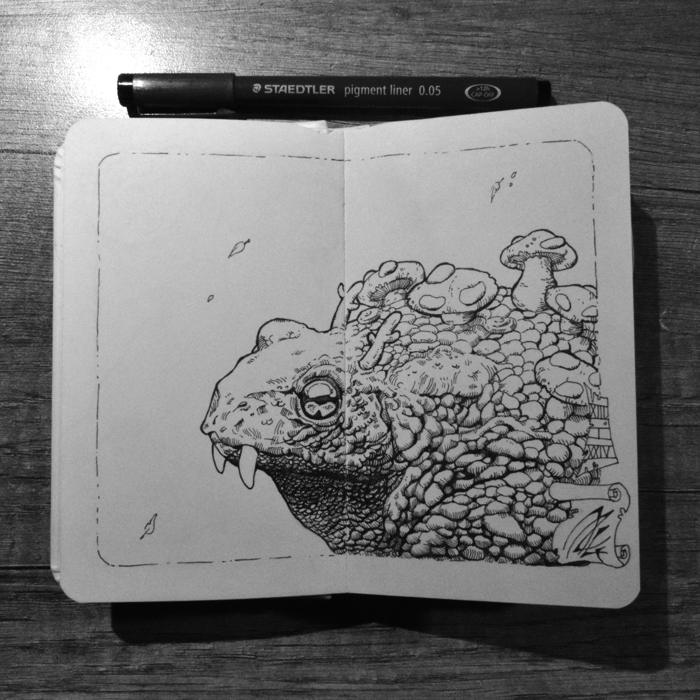 Dessin dans un petit carnet d'un dinosaure imaginaire à l'aspect d'un gros crapaud avec des dents de sabre et des petites cornes mignonnes. Des champignons poussent sur son large dos