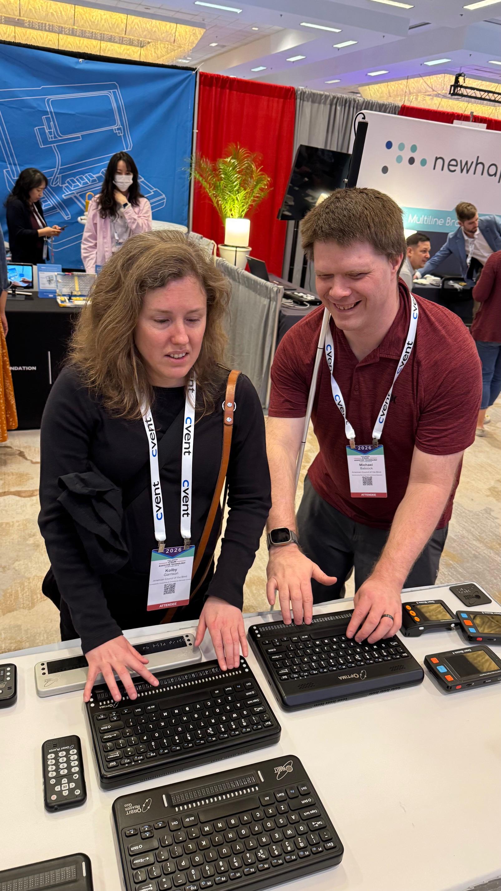 Kolby Garrison (left) and Michael Babcock (right) trying out the Optima device at Orbit’s booth at the CSUN Assistive Technology Conference. 