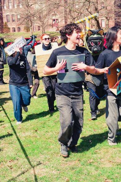 In the foreground a number of lightly costumed people walk past me on a grassy lown,  behind them there is a person wearing a partial fursuit with a wolf mask with red eyes who seems to be looking right at me.  talk about a missed connection.
