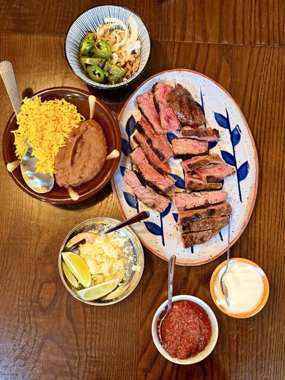 Fajitas on a plate seen from above with various accoutrements (sour cream, cheese, onions, jalapeños, salsa, rice, and refried beans)
