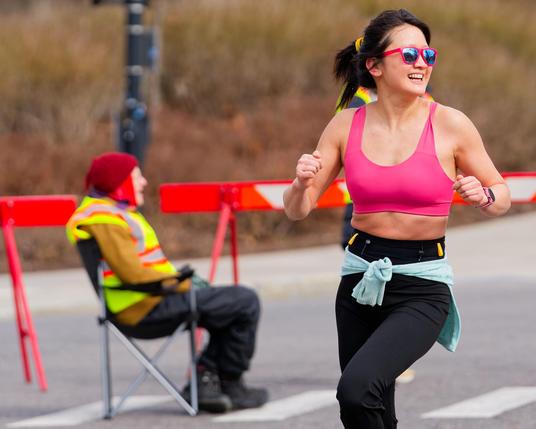 Asian woman with pink tank top and pink shades and charcoal gray pants looking to right with high-viz volunteering and barricades in background