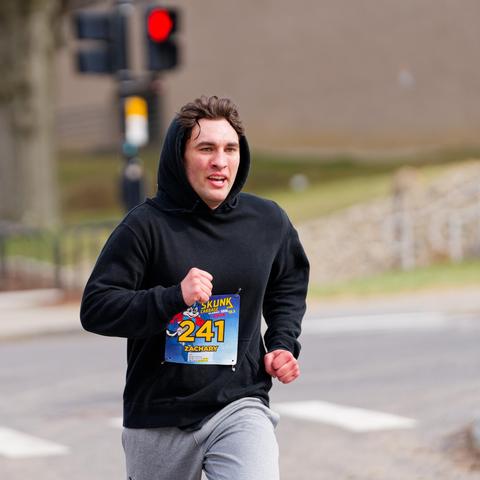 Young man in black hoodie and light grey pants runs through intersection with red pedestrian signal in background