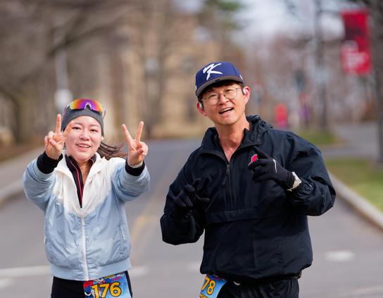 Asian woman making double-V hand sign wearing light colored jacket next to asian man wearing a dark jacket