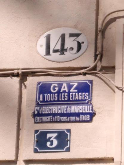 Zweierlei Hausnummern in Marseille, sowie Schilder, die stolz Gas & Strom auf allen Etagen verkünden.