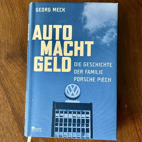 Titelbild des Buches "Auto. Macht. Geld. Die Geschichte der Familie Porsche Piëch" von Georg Meck. Vor einem blauen, fast wolkenlosen Himmel ist im unteren Drittel ist das obere Ende eines Büro-Hochhauses zu sehen, oben drauf ist ein großes VW-Logo montiert. Oben rechts in der Ecke sieht man ein kleines Stück Wolke. 