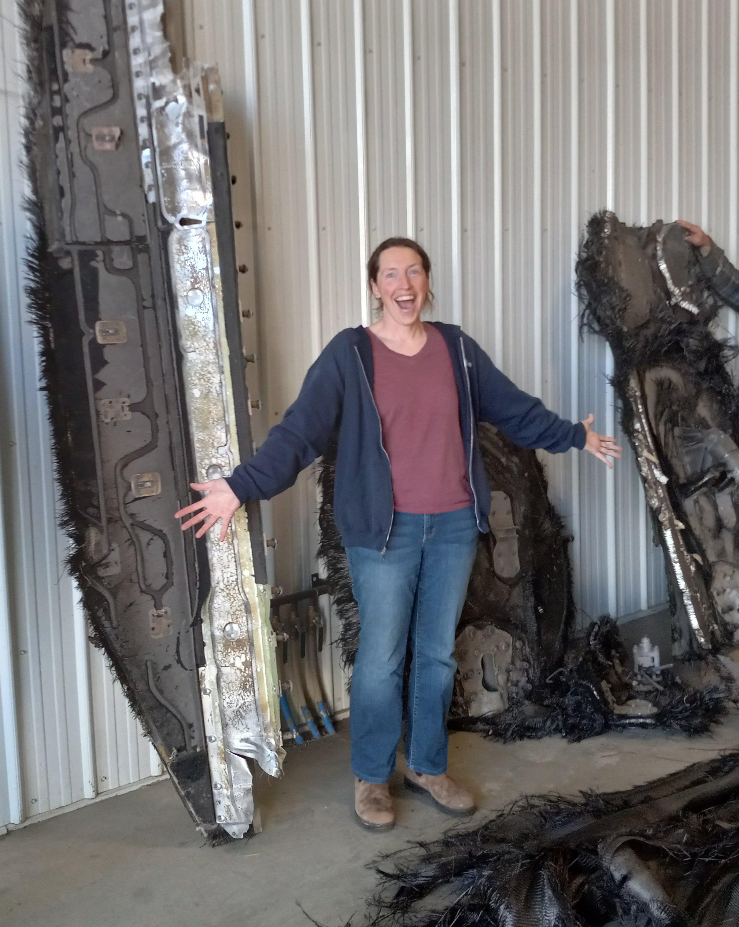A photo of me, looking very excited with my arms outstretched, with multiple extremely large pieces of space debris (bigger than me) from a SpaceX Crew Dragon Trunk that fell on farmland in Saskatchewan in 2024.