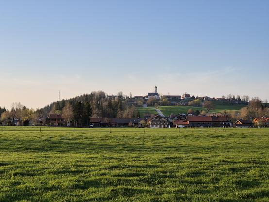 a green meadow with a hill in the back.
A village is at the foot of the hill a church on top.
Blue sky