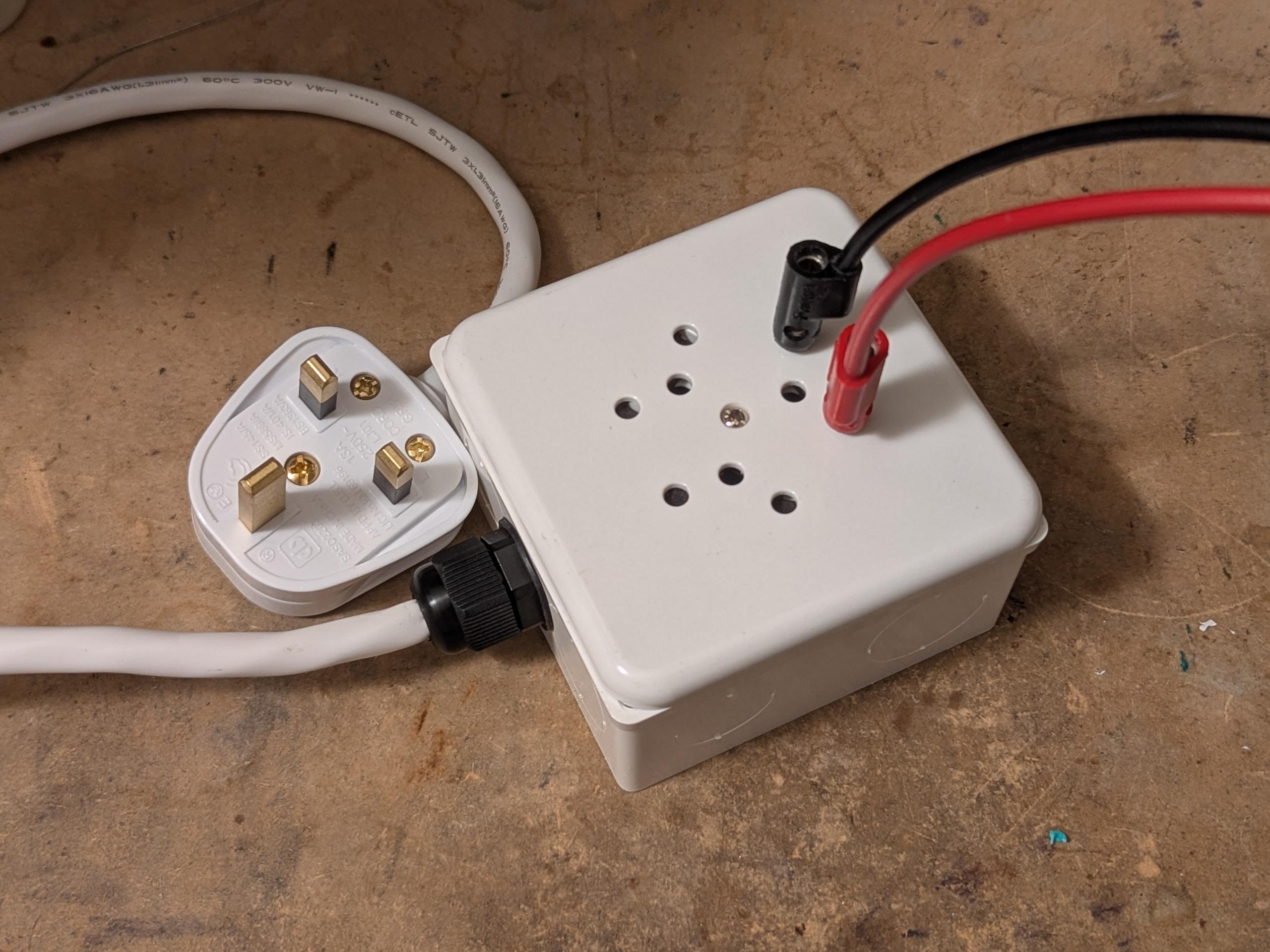 British plug with a wire going to a 86mm electrical box with a Swiss triple 3-pin outlet that is now illegal there because it isn't recessed. two banana cables are plugged into one of the outlets.