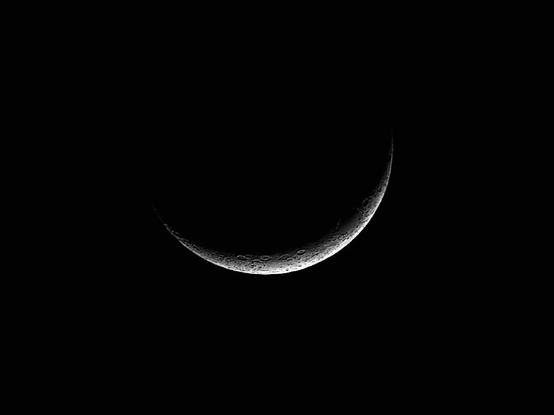 A crescent moon hangs in a clear, dark night sky, its lit crescent surface detailed with craters and shadows.