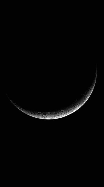 A crescent moon hangs in a clear, dark night sky, its lit crescent surface detailed with craters and shadows.