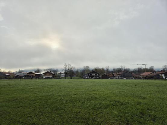 A green field, houses and trees in the background. Low hanging clouds