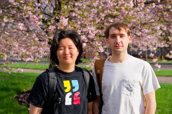 Asian woman with black hair with colorful quotes on the left and white man with brown hair and white shirt stand under puffy pink flowers