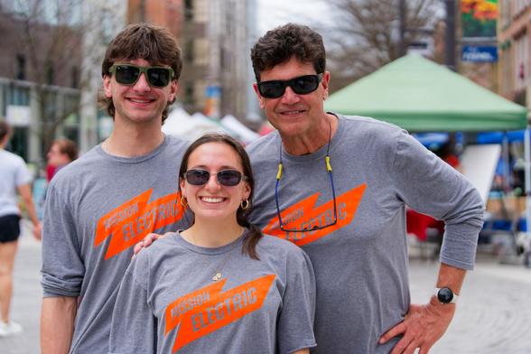 Two men and a woman all wearing grey shirts with an orange MISSION ELECTRIC Logo