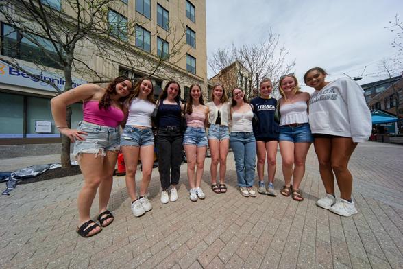 Nine girls face me in a semi-circle on a cream colored brick surface with Beginnings Credit Union, bare trees and other buildings in background.