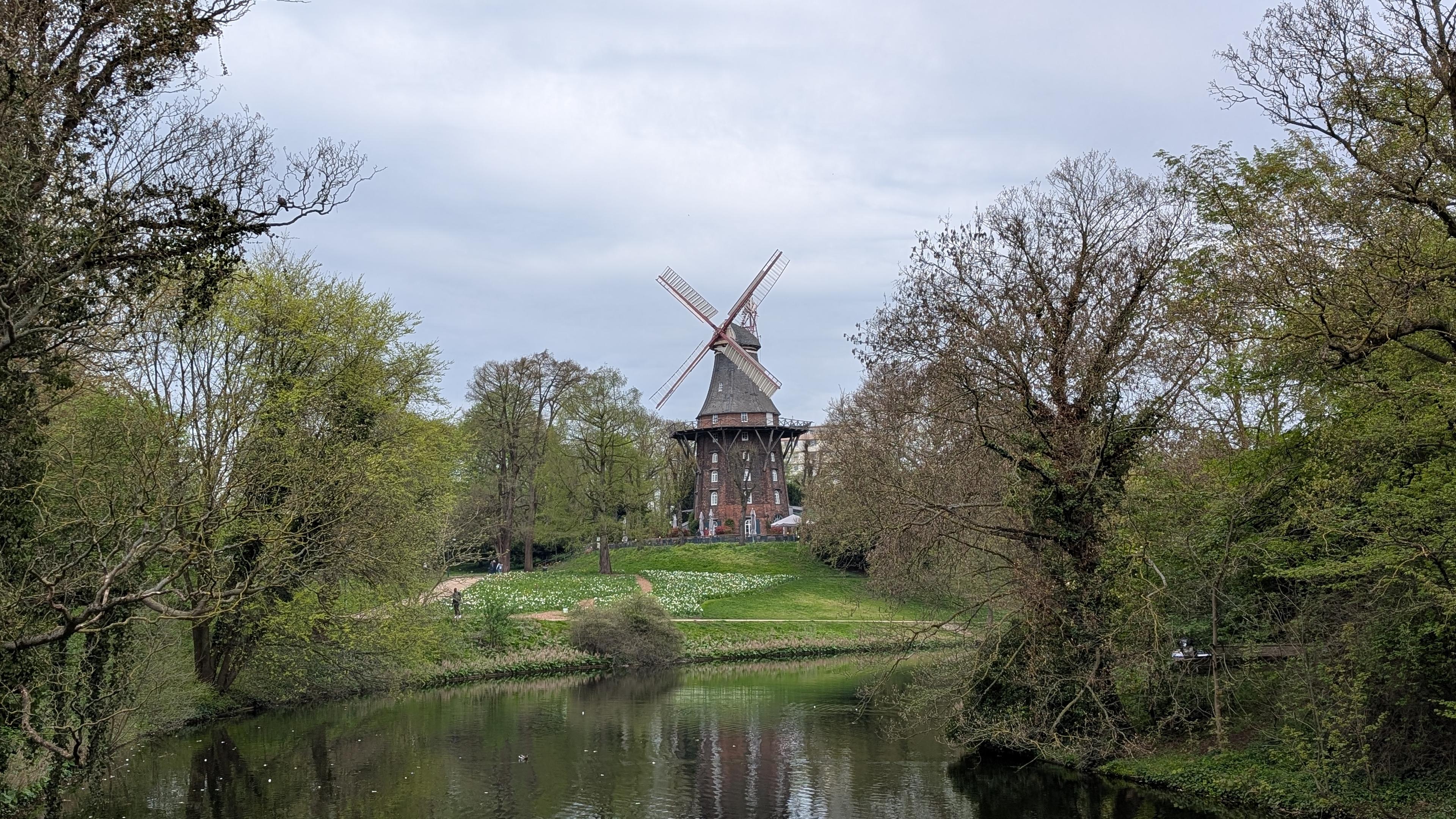 Historical windmill "Am Wall" seen from a bridge crossing a moat, lots of greenery