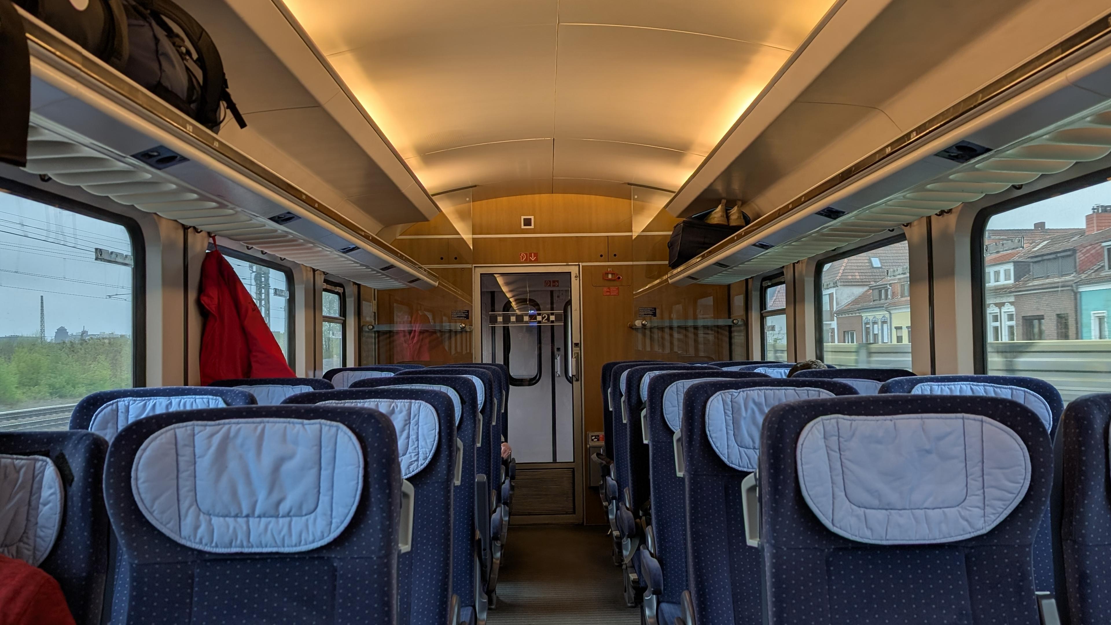 Interior of the IC 1 coach, 2+2 seating configuration, blue seats, light-blue headparts, wooden-like panelling at the end, only few passengers