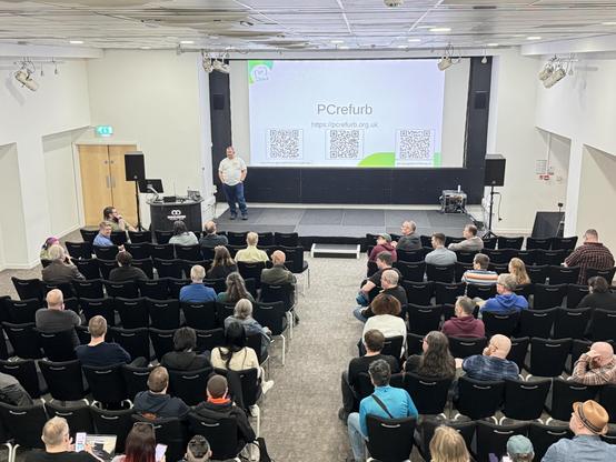 Jon Spriggs on stage at OggCamp 2026 in front of an audience in Manchester