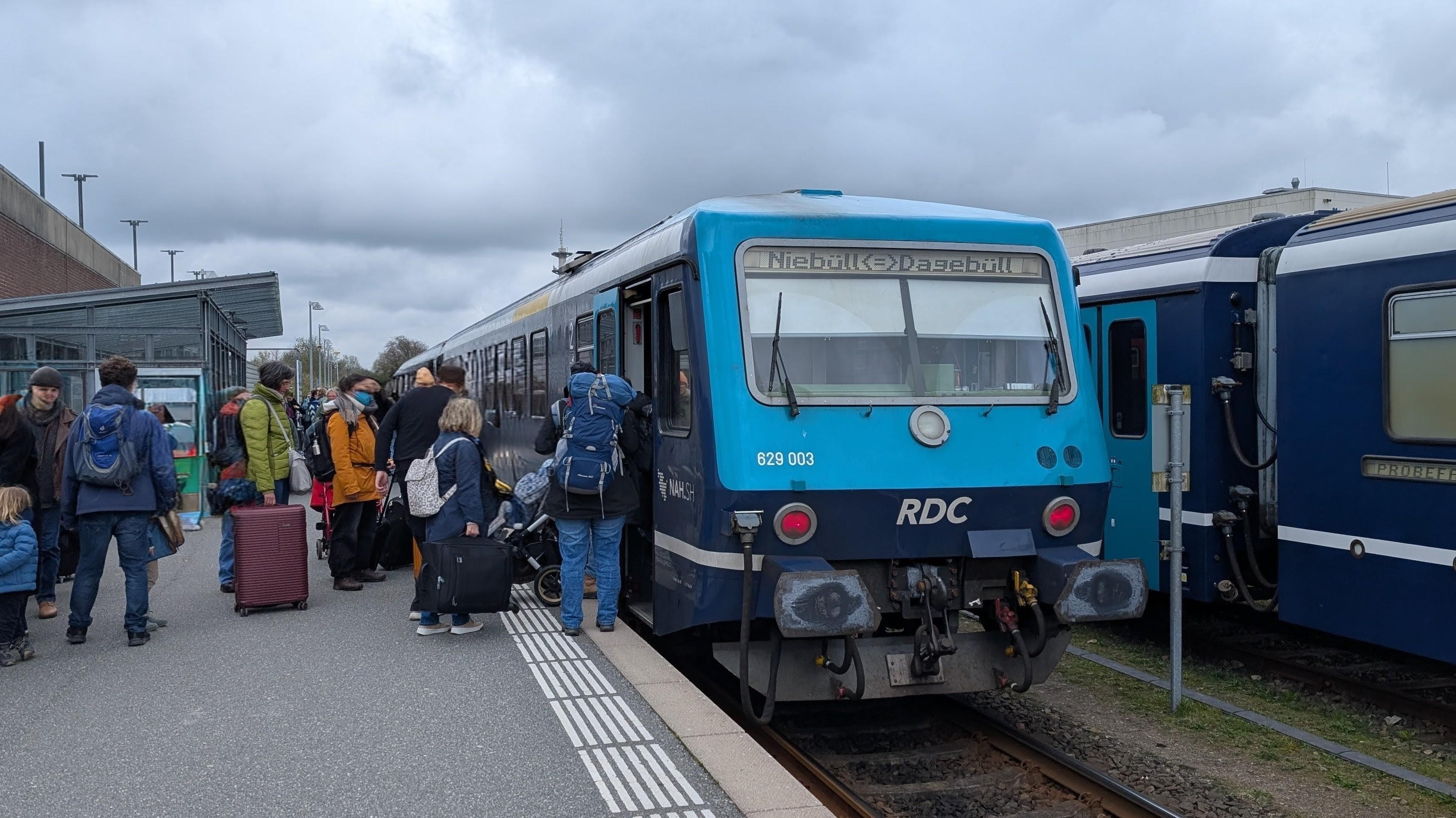 Many passengers boarding an RDC Class 628 DMU with Schleswig-Holstein at Niebüll NEG, open doors, one platform, another train in the background (edited picture: faces removed or anonymised)