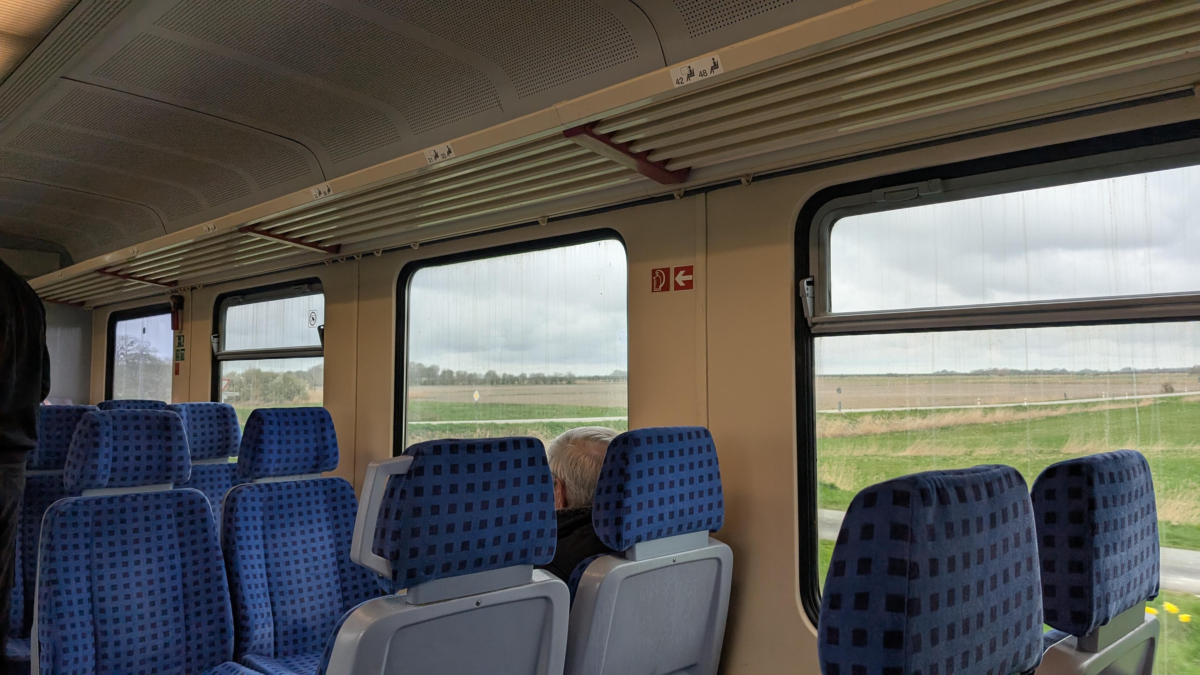 Interior of the train, 2+2 seating configuration, blue seat pads, flat fields outside, some trees