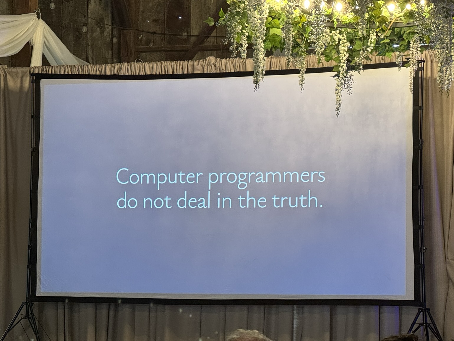 a conference slide projector showing the phrase “computer programmers do not deal in the truth”