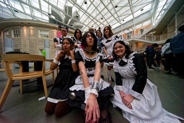 Roughy 7 men and woman look resplendent in black and white maid costumes seen in an ultra wide angle shot showing the sky through a space frame