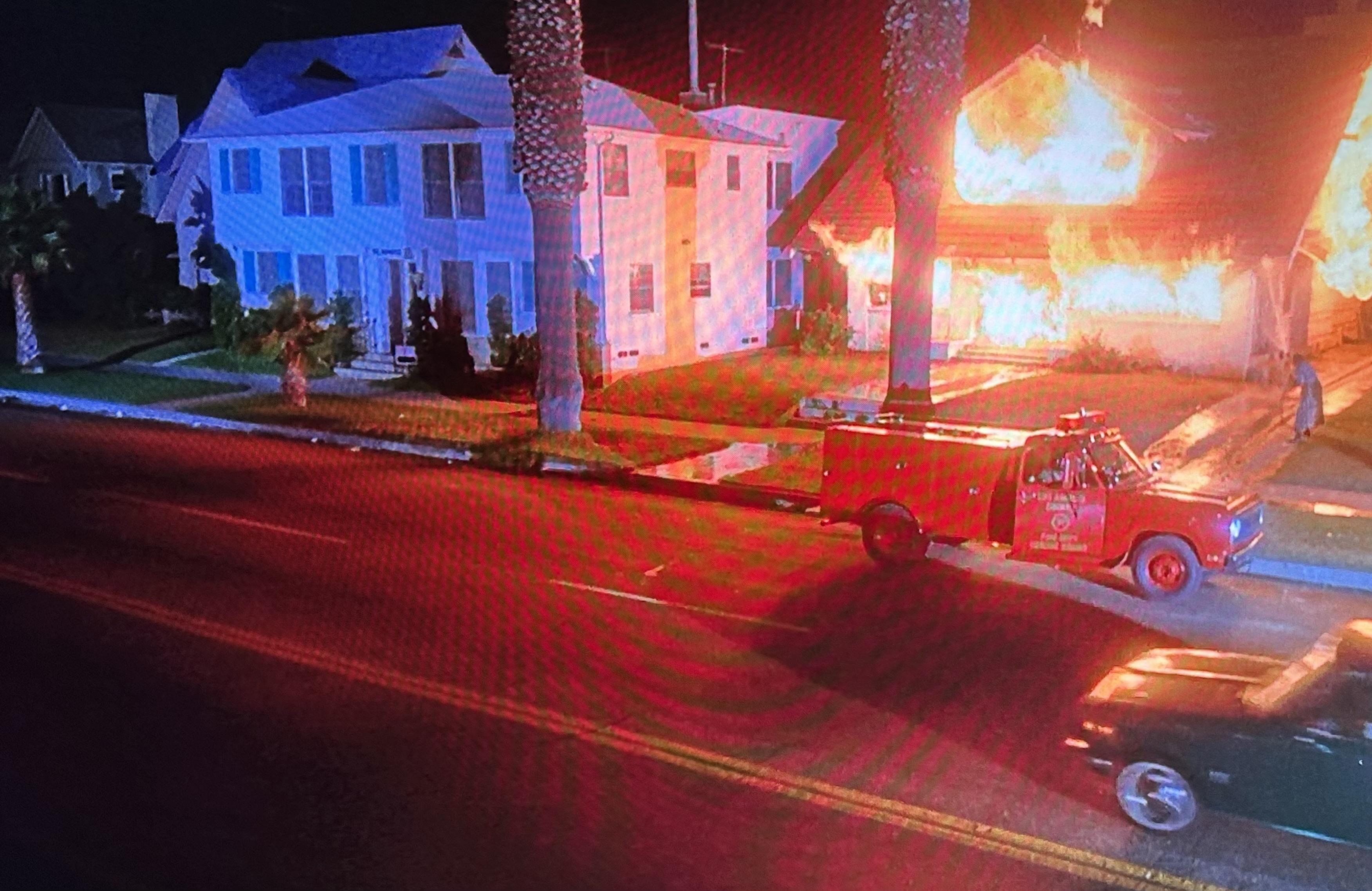 A home is fully engulfed in flames on an open LA street with a second house no more than 10 feet away. squad 51 has just rolled up.