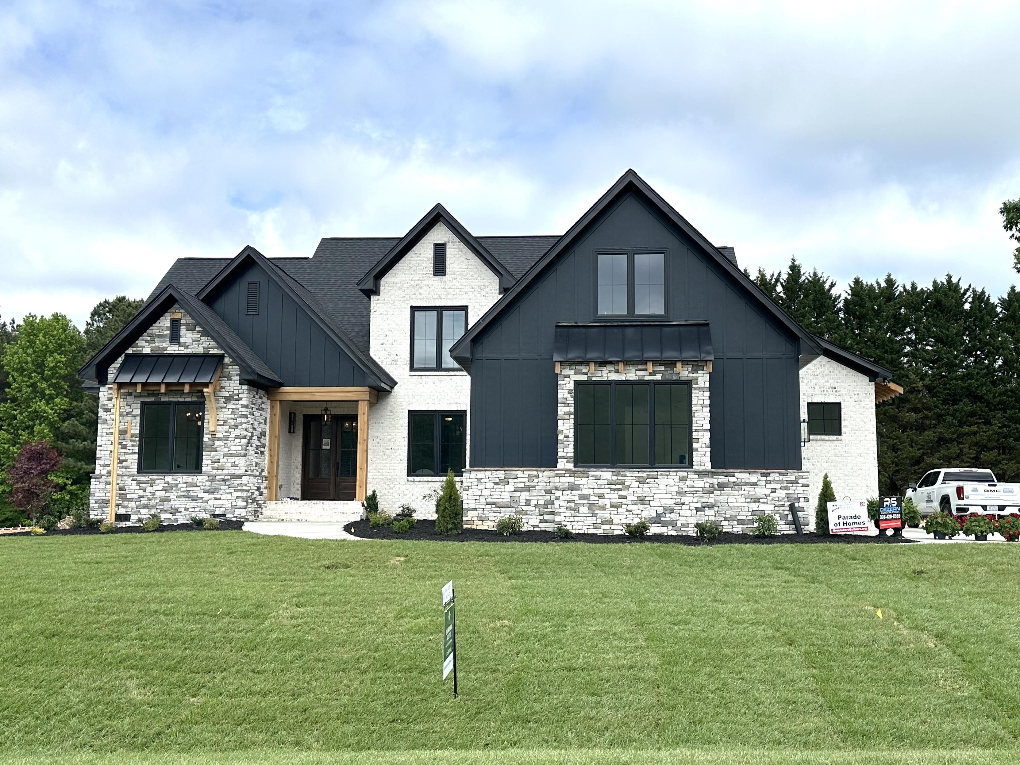 A large gray stone home with black and grey painted roofline sitting on a grassy hill.
