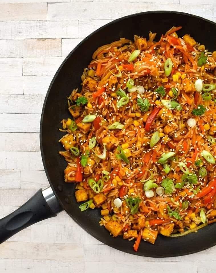Tofu fried rice in a pan topped with spring onion (green onion) and sesame seeds.