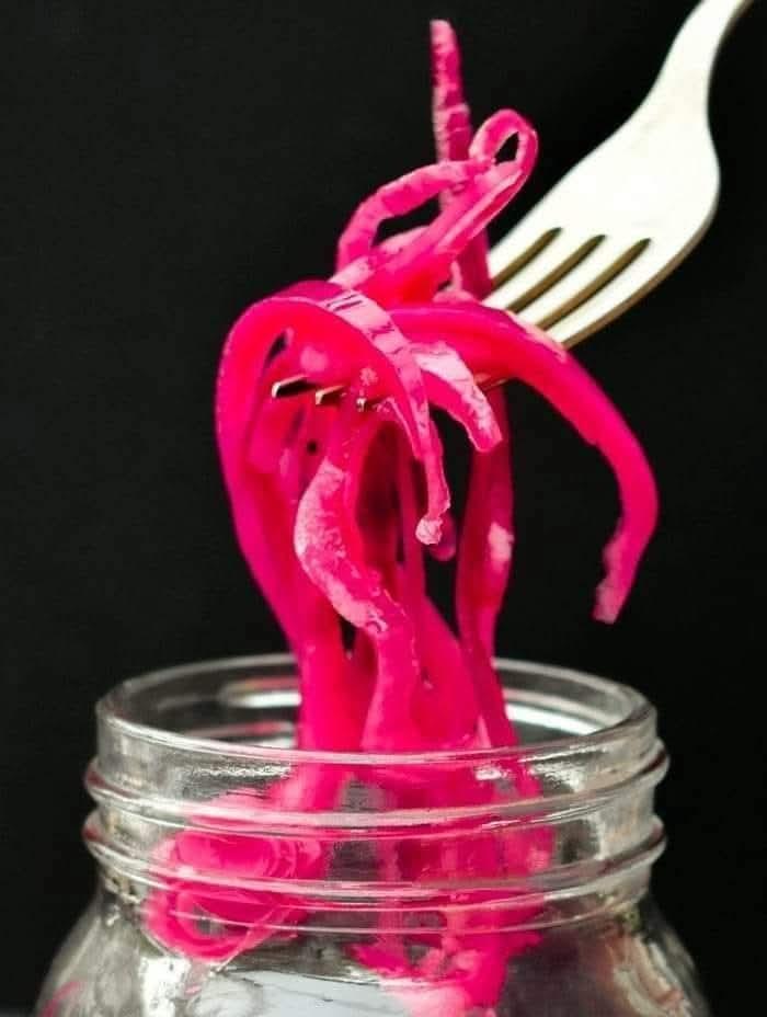 Red pickled onions slices lifted out of a jar with a fork.