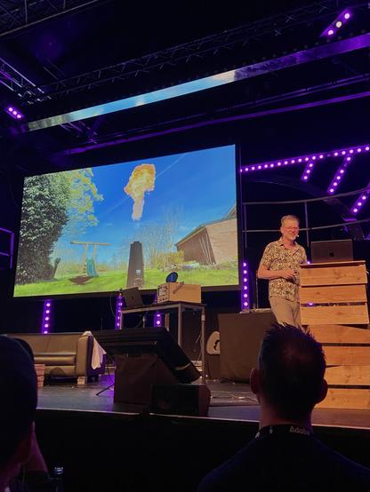 Niels Leenheer on stage, behind him a video of a flamethrower going off