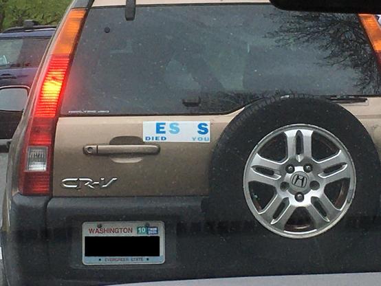 A brown Honda CR-V with a Washington license plate. It has a single bumper sticker, which originally likely said “JESUS DIED FOR YOU” in rainbow letters, but is now so faded that only some of the colors remain, making it say “ES S DIED YOU”