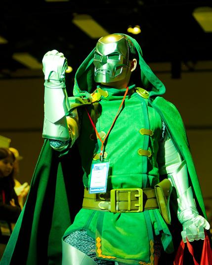 Man with Green Coat Under Green Lights Looks defiant with gauntlets and metal mask in dark convention center
