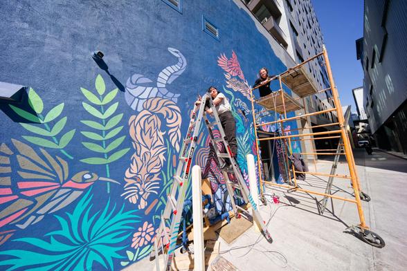Two girls on ladder and scaffold paint undersea mural on dark blue wall