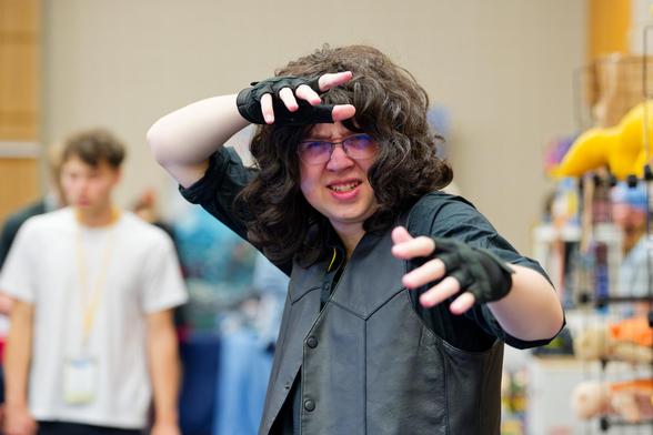 Man with dark grey shirt, fingerless glove and lots of wave hair makes martial arts stance on floor of comic book conference