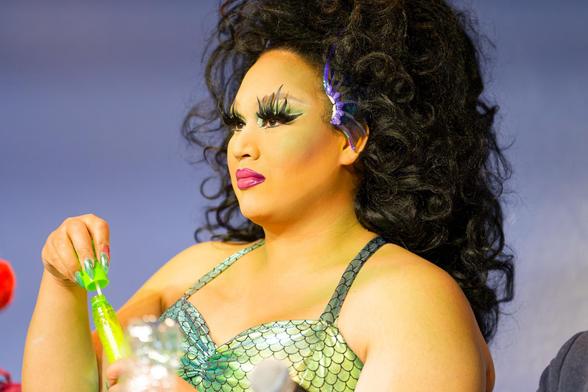 A mermaid (I think in drag) with a huge black curly wig and big eyelashes