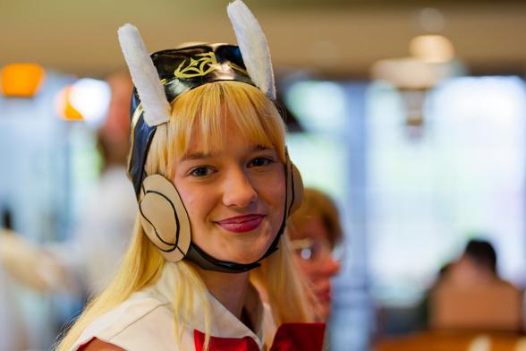 Rather nice headshot of blonde girl with bridle-like headgear with dining area lit with lights and windows behind her