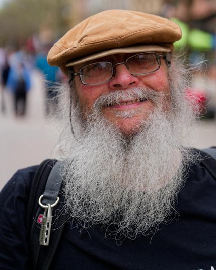Man with black shirt, tan beret and lots of white beard with defocused blobs in background
