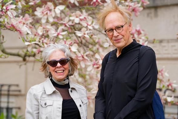 Shorter women with short white hair and dark classes and taller man with mostly blonde hair with magnolia tree behind them