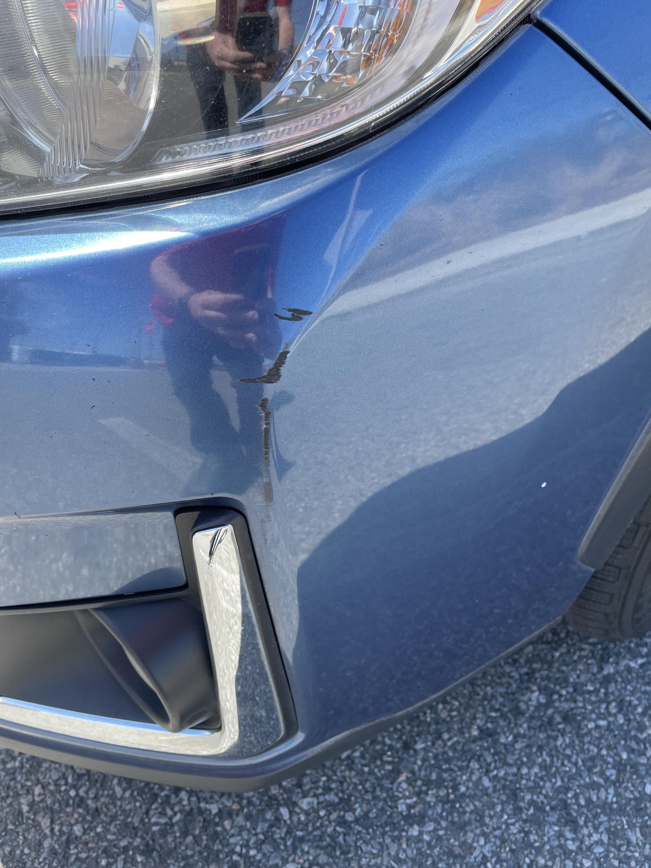 A blue car bumper missing paint caused by a collision with another vehicle. The owner of this vehicle did not cause that incident but is the victim of it.