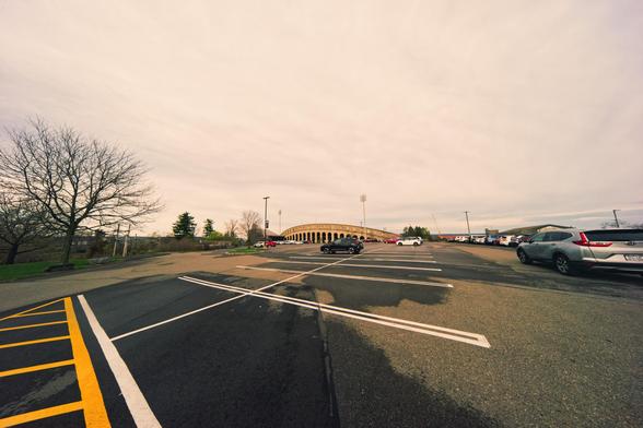 A curved structure on the horizon looks simultaneously small and massive at the end of a mostly empty parking lot