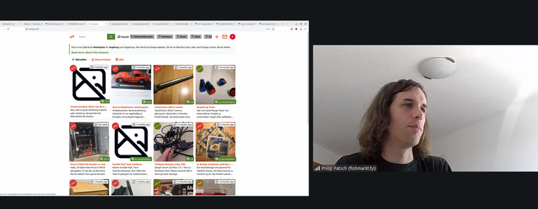 A browser showing austa.social, a federated marketplace (Marktplatz) for Augsburg and surrounding area, displaying a grid of secondhand listings including shoes, toy cars, a 3D printer, an enamel pot, a Thinkpad charger, and arcade buttons. Philip Patsch of flohmarkt.fyi is visible speaking in the video panel on the right.