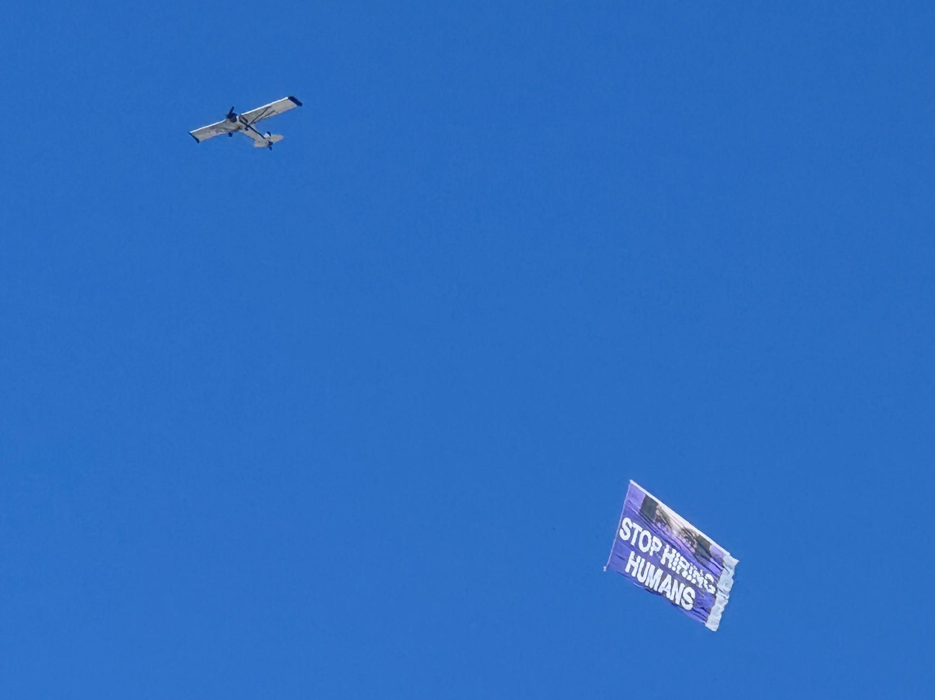 A low flying plane hauling a big banner that says “Stop hiring humans”. This is the marketing slogan of an AI startup. 