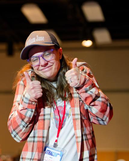 Woman with "William Jane" Billed Cap and Flannel  shirt gives double thumbs up
