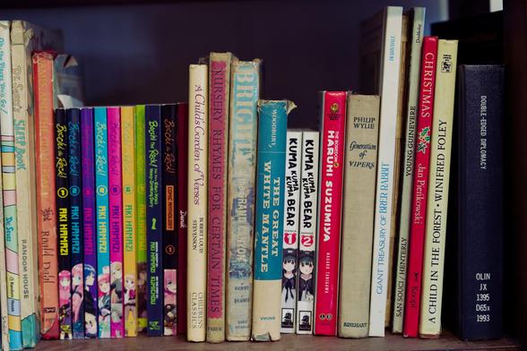 Collection of books including Dr. Suess, Bocchi the Rock, western children's books, the Great White Mantle (about glaciers), Kuma Kuma Kuma Bear, Haruhi Suzumiya, Generation Of Vipers with a single library book DOUBLE-EDGED DIPLOMACY on the far side
