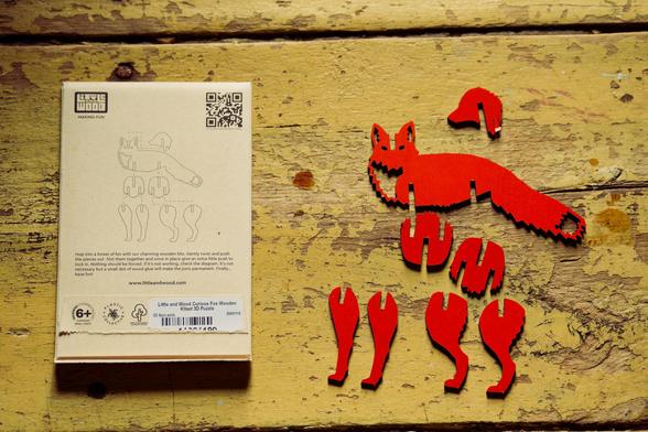 On the left a beige package with barcodes and visual assembly instructions for a fox model that has had flat parts pressed out and assembled on a yellow wood floor.