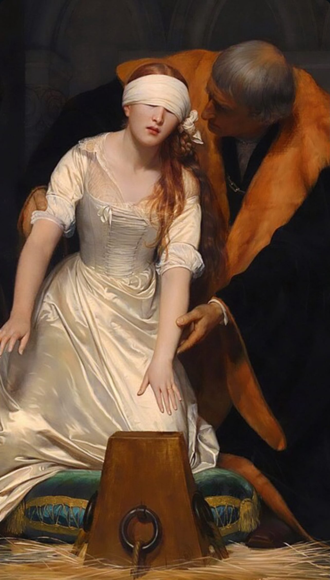 A close-up of a classical oil painting depicting a young woman with long reddish-blonde hair, blindfolded with a white cloth. She wears a pale satin dress and kneels on a green cushion, reaching her hand toward a wooden block. An older man in a dark robe with a fur-lined collar leans toward her, guiding her arm.