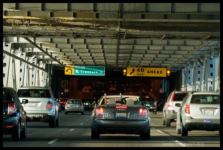 We are in the 3rd from the left of 4 busy lanes of a bottom level of a bridge.  Ahead, it looks like we are about to enter a dark tunnel.