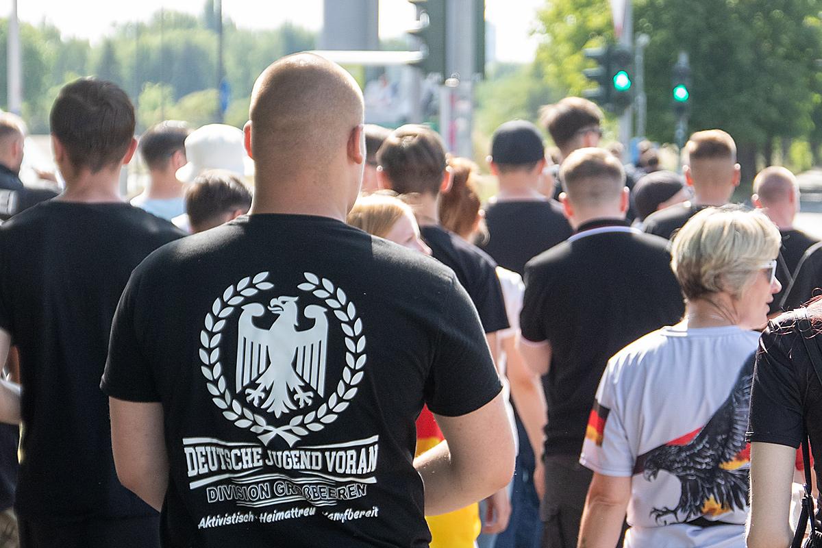 Personen von hinten auf einer Demo, eine Person mit kahlrasiertem Schädel trägt ein Shirt mit der Aufschrift "Deutsche Jugend voran"